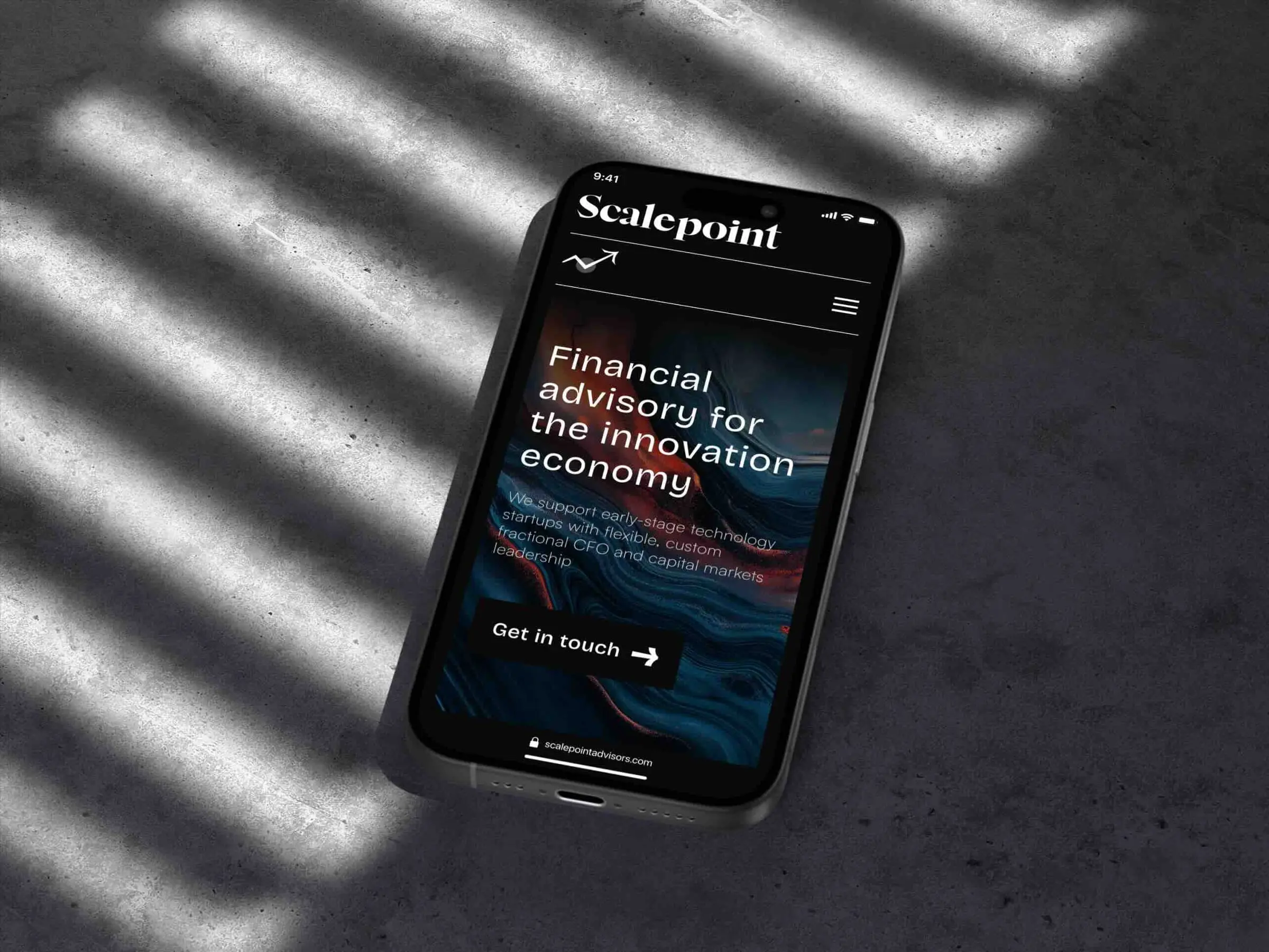 A phone lying on grey concrete in slatted daylight, showing the site's hero over a dark marbled image