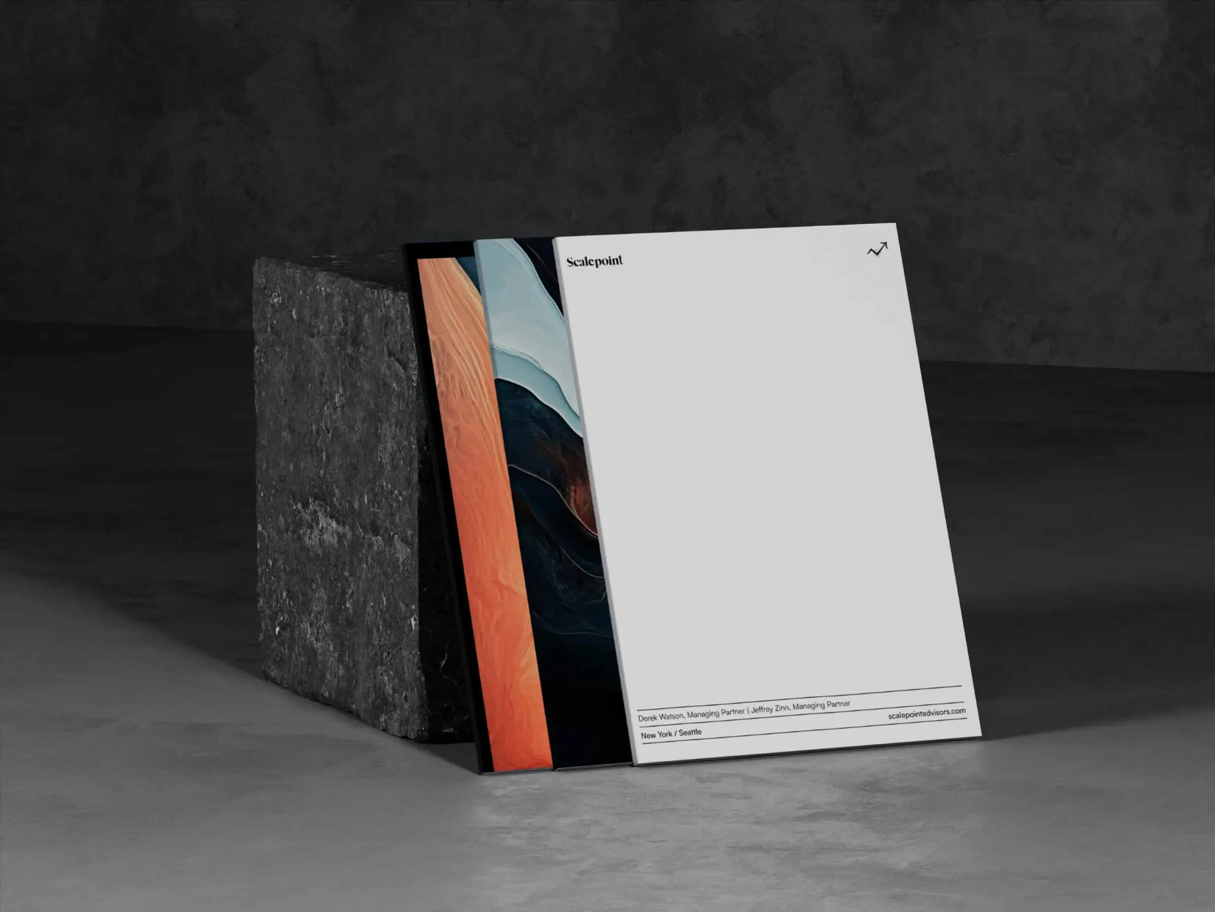 A letterhead and a folder printed with an orange and navy abstract, leaning against a concrete block in a dark studio